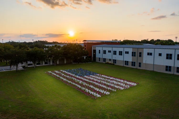 Aerial view of an American flag made of small flags on a school lawn at sunset.