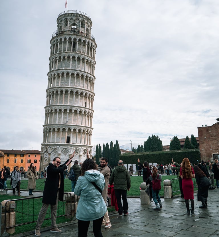 Tourists posing for photos in front of the Leaning Tower of Pisa in Italy on a cloudy day.