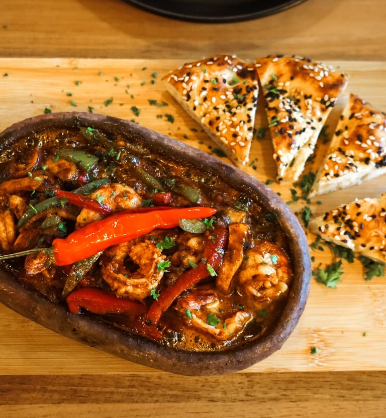 Spicy shrimp stew served in a traditional clay pot with sliced sesame bread on a wooden board.