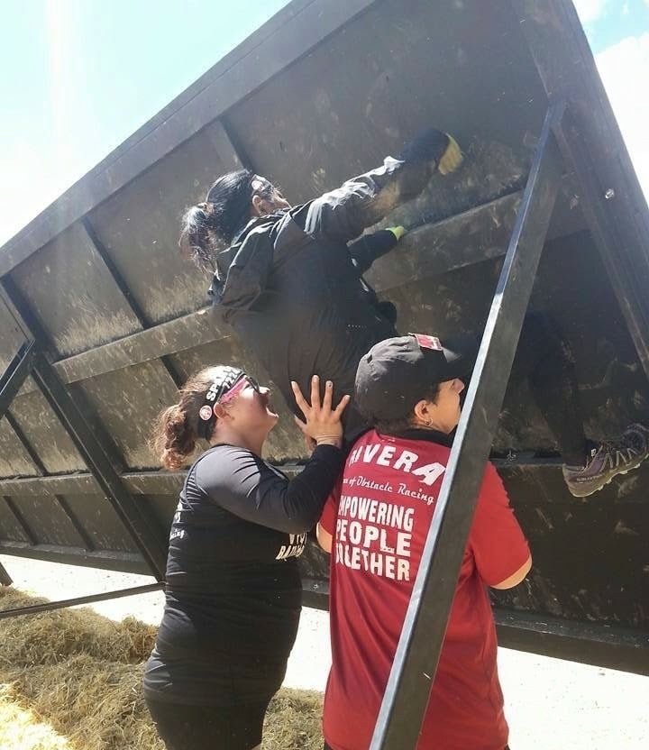 Members of women of racing helping female athlete over inverted wall