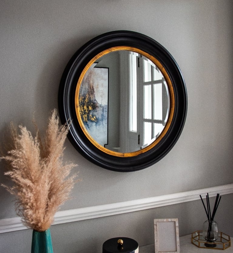 Wall with a mirror featuring a black frame and gold lining, above a shelf with decorative pieces
