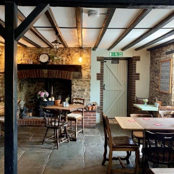a table and chairs near to a wood burning fire with a clock above it