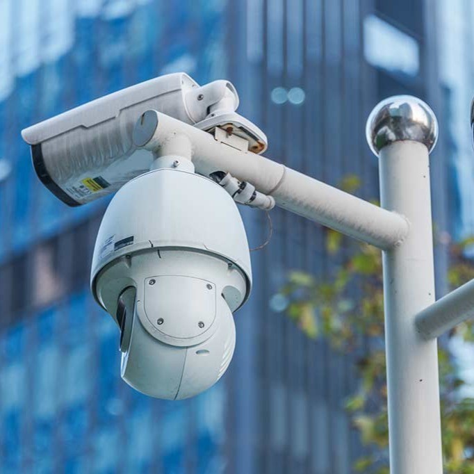 White outdoor PTZ dome security camera and bullet camera mounted on a pole for building surveillance.