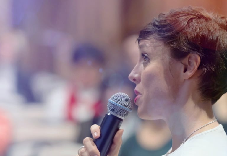 a-female-business-executive-holding-a-microphone-addresses-group