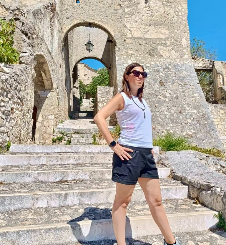 A woman in sunglasses standing on stone steps in an old Italian village with ancient arches.