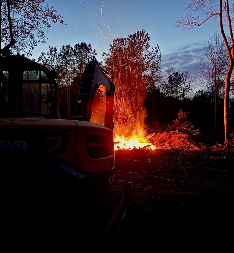 Excavator in foreground watching over burn pit at night
