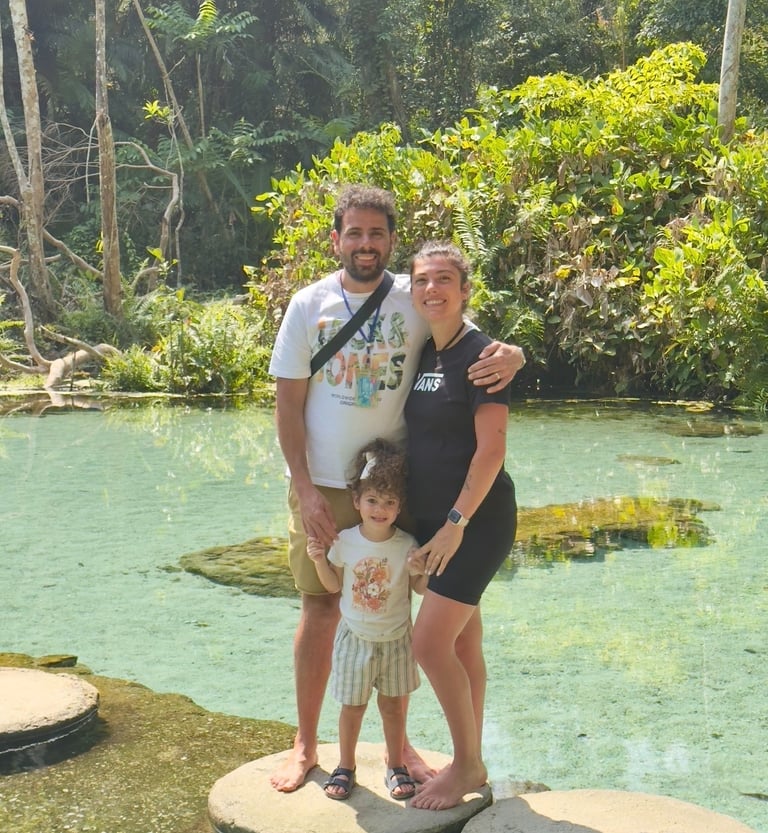 A happy family of three poses on stepping stones in a clear tropical lagoon surrounded by lush jungle.