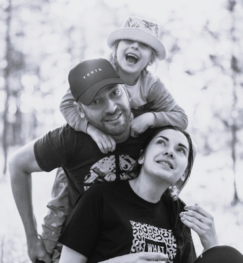 a picture of a father, mother and child who is piggy backing on the father's back smiling