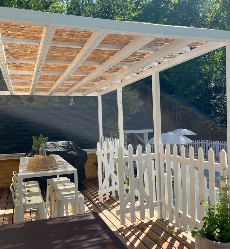a patio with a pergola,  table and chairs and a grill
