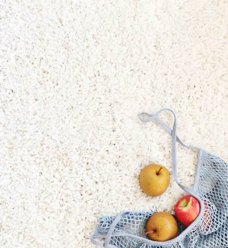 a bag of apples in a mesh bag on clean white carpet