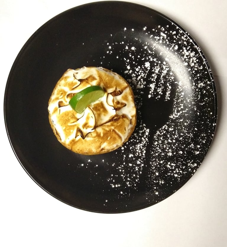 Black plate with individual dessert, containing outline of a fork and fresh lime