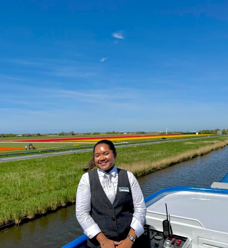 Smiling beautiful crew in staff uniform on a cruise ship passing colorful Dutch tulip fields.