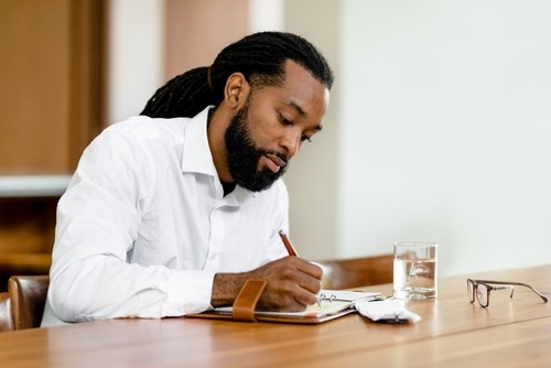a man in a white shirt and glasses is writing in a journal