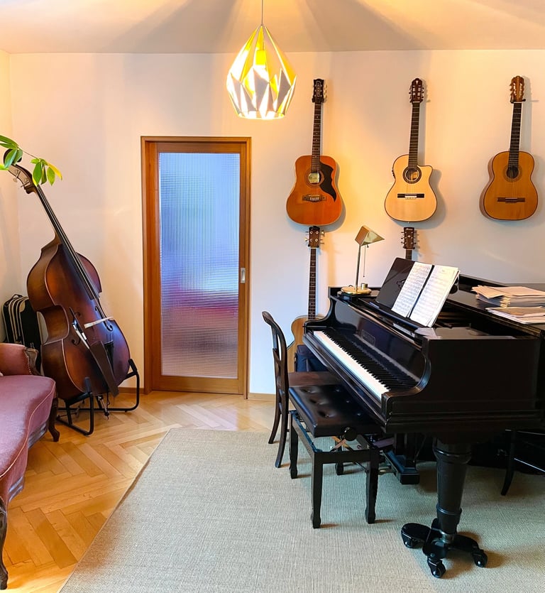 ein heller Unterrichtsraum mit einem Flügel, einem Kontrabass und mehrere Gitarren, die an der Wand