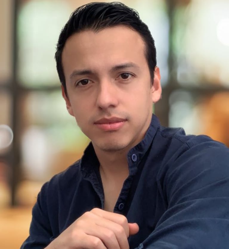 Professional portrait of a young man with dark hair wearing a navy blue button-down shirt.