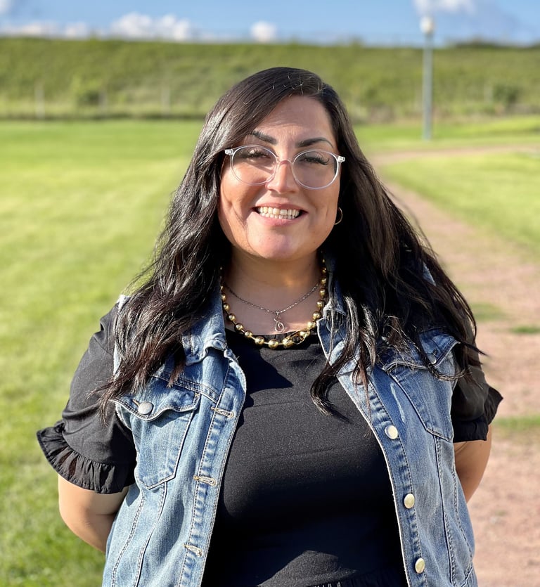 Smiling woman with dark hair and glasses wearing a denim vest. Cristina Adame