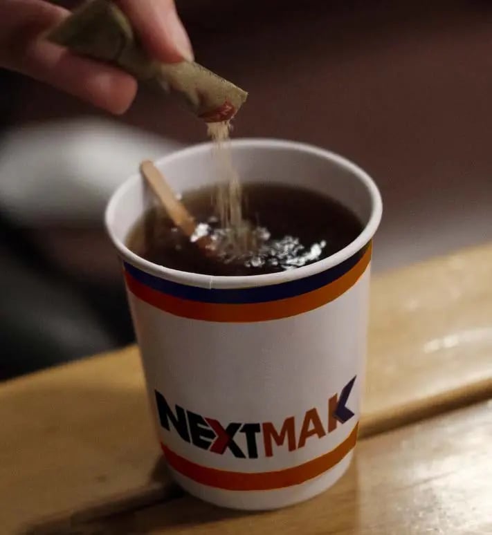 sugar stick pack pouring at a tea cup with NEXTMAK logo