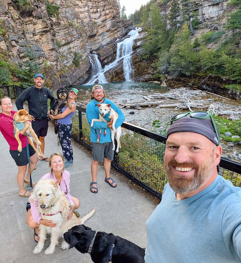 Travel group with their dogs smiling at Cameron Falls waterfall in Waterton, Alberta.