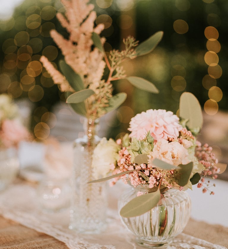 Elegantes Tischgesteck für die Hochzeit mit rosa Blumenarrangements in Glasvasen und warmem Bokeh