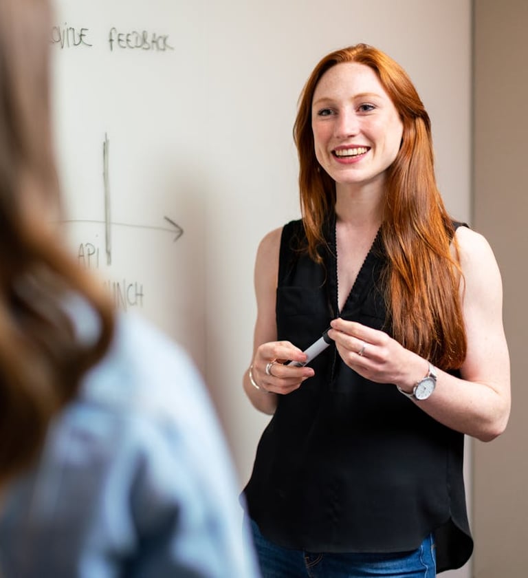 a woman in a black top and jeans standing in front of a white board
