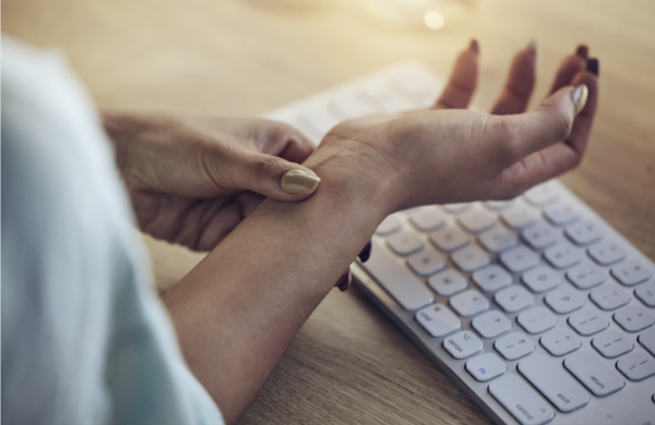 A person holding their painful wrist over a keyboard, illustrating carpal tunnel syndrome and RSI symptoms.