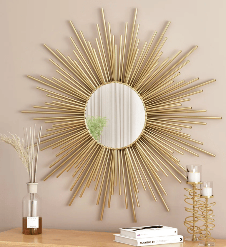 Elegant gold sunburst wall mirror hanging above a table with candles and a glass vase decor.