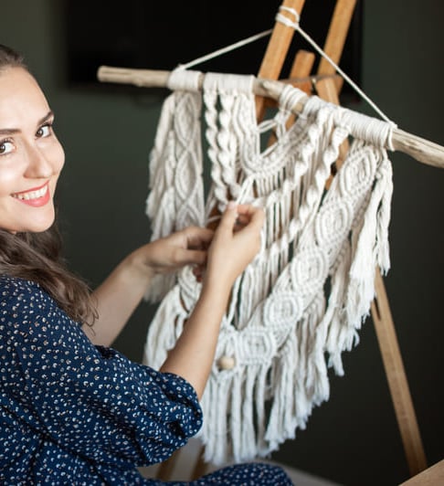 mujer sonriendo a la camara, y trabajando en un proyecto de macrame