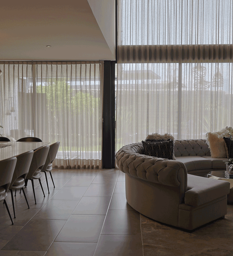 Sala-comedor con cortinas traslúcidas de doble altura, sofá en escuadra y mesa de mármol | KARÄNA
