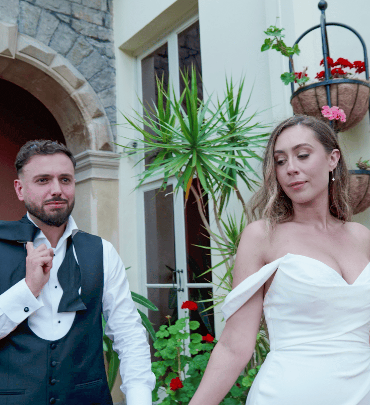 A bride and groom joyfully walking surrounded by floral decorations and smiling guests.