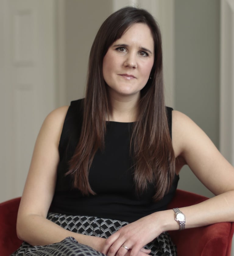 Photo of Anna Joyce, CBTI insomnia therapist in UK, sitting in red chair wearing a black dress