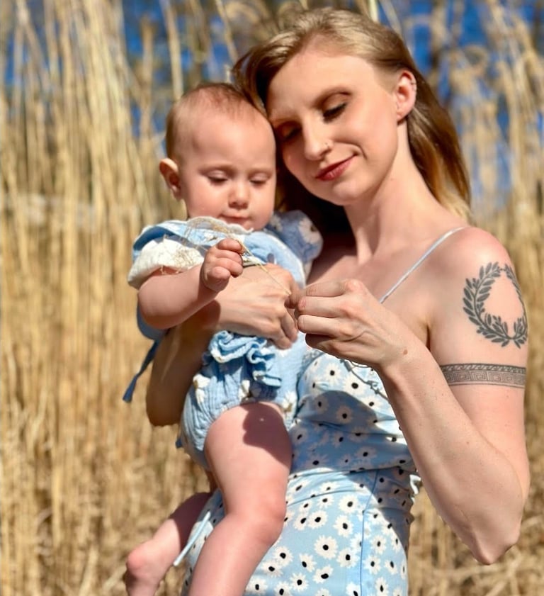 A mother and baby girl both wearing matching blue dresses in a hay field on a sunny day, symboling maternal love.