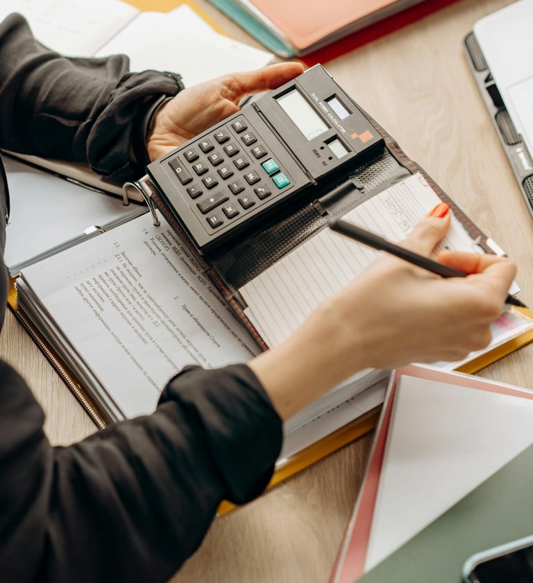 Mãos usando calculadora e caneta sobre documentos para análise fiscal e tributária
