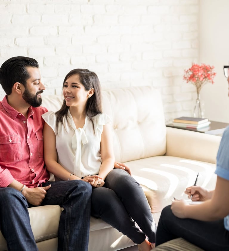Couple sitting close together, smiling at each other during a EFT for couples therapy session with a therapist taking notes