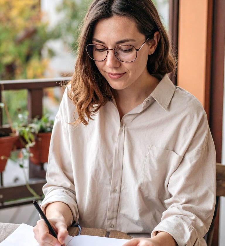 Woman writing in a notebook about her feelings while sitting near a window