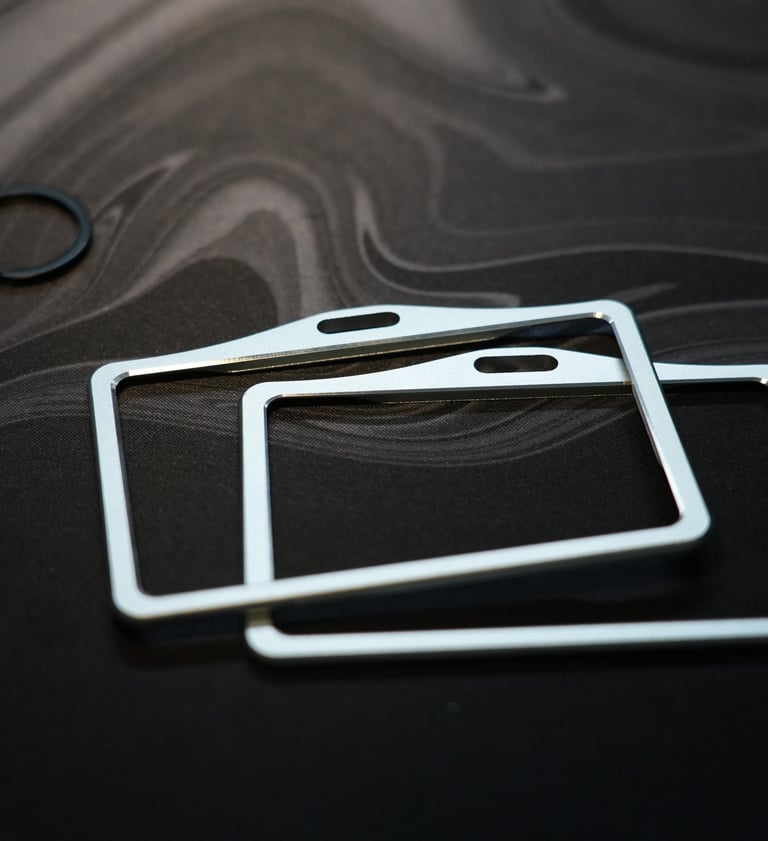 Two brushed metal ID badge holders on a dark marbled surface.