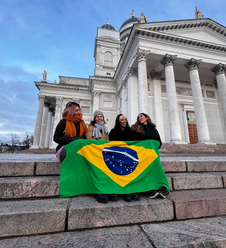 Quatro fundadoras do BiF sentadas na escadaria da Catedral de Helsinki,  com a bandeira do Brasil cobrindo as pernas