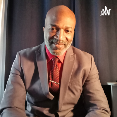 A smiling man posing in a sitting position wearing a grey suit and red tie 