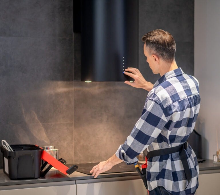 A technician in a blue and white plaid shirt repairing a black kitchen chimney hood