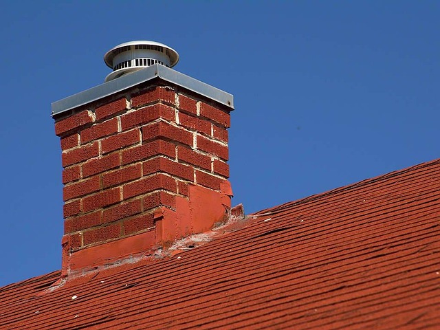 red brick chimney with a metal cap on a red tiled roof against a clear blue sky