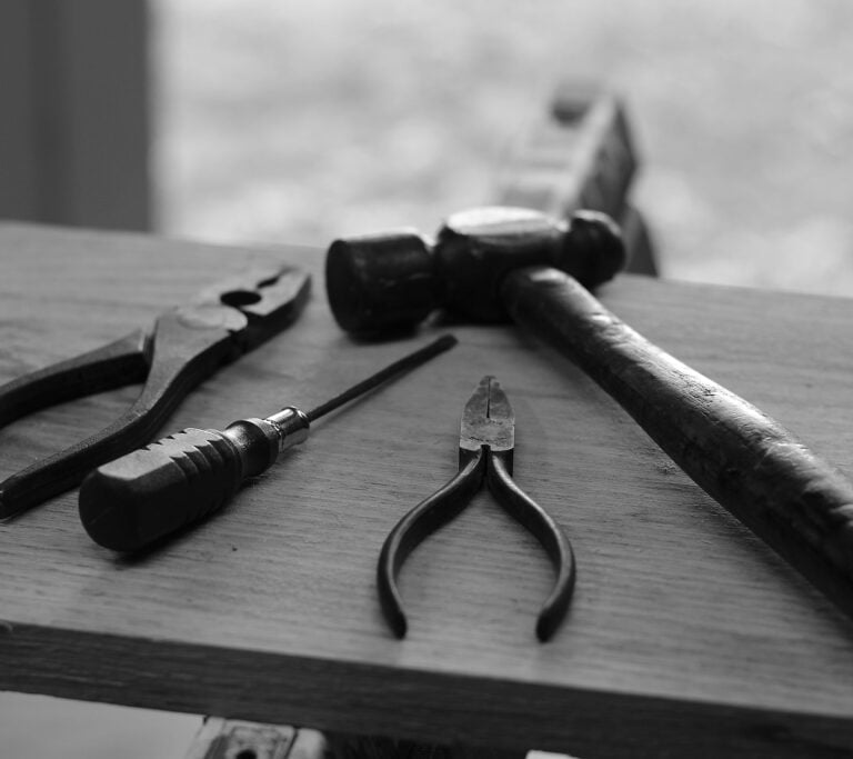 various tools, including pliers, a screwdriver, and a hammer, resting on a wooden surface
