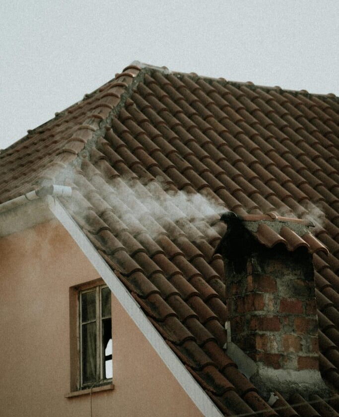  A chimney on a tiled roof with smoke coming out, on a cloudy day