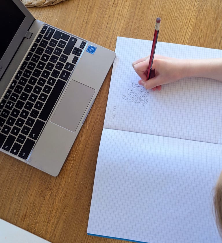 Child writing in an exercise book whilst doing their online tuition to help them with the 11+ test
