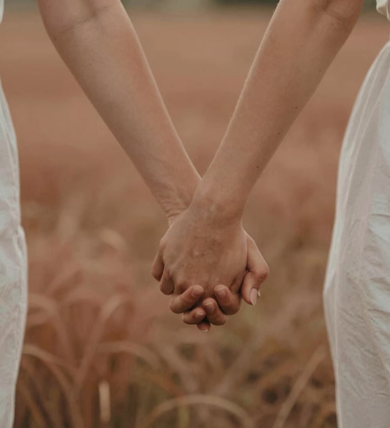 A close-up of a couple's hands interlaced while walking through a field, shot in warm cinematic light with natural focus, incorporating soft terracotta and sand tones in the environment.