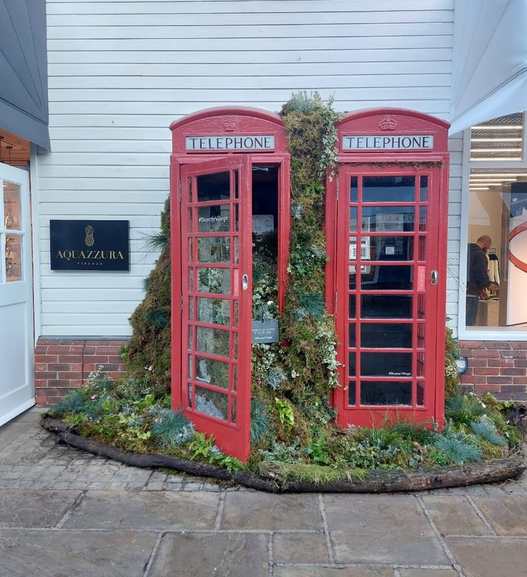 Red British telephone boxes filled with lush green plants and moss in a floral outdoor display.