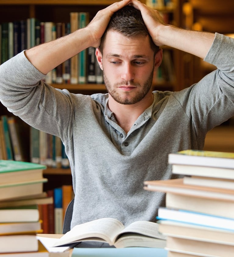 Studente con le mani tra i capelli in segno di frustrazione; intorno libri aperti e chiusi