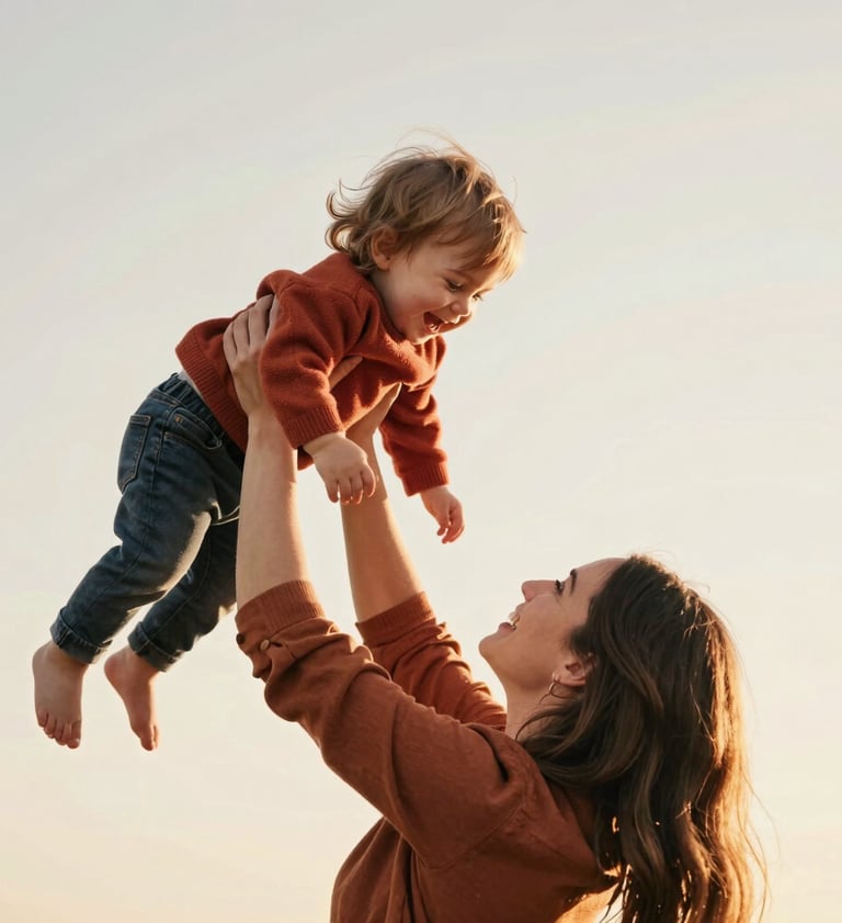A medium shot of a mother lifting her toddler in the air, both beaming with joy. The scene is bathed in sun-drenched warmth, with the child wearing a terracotta-colored sweater against a soft off-white sky.