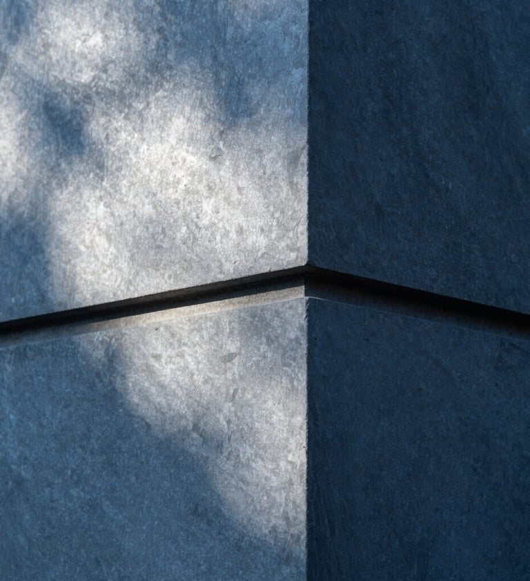 Close-up of an architectural detail featuring slate blue concrete and sharp edges. Light and shadow create a geometric pattern of soft cloud white and deep obsidian. Industrial and premium feel.