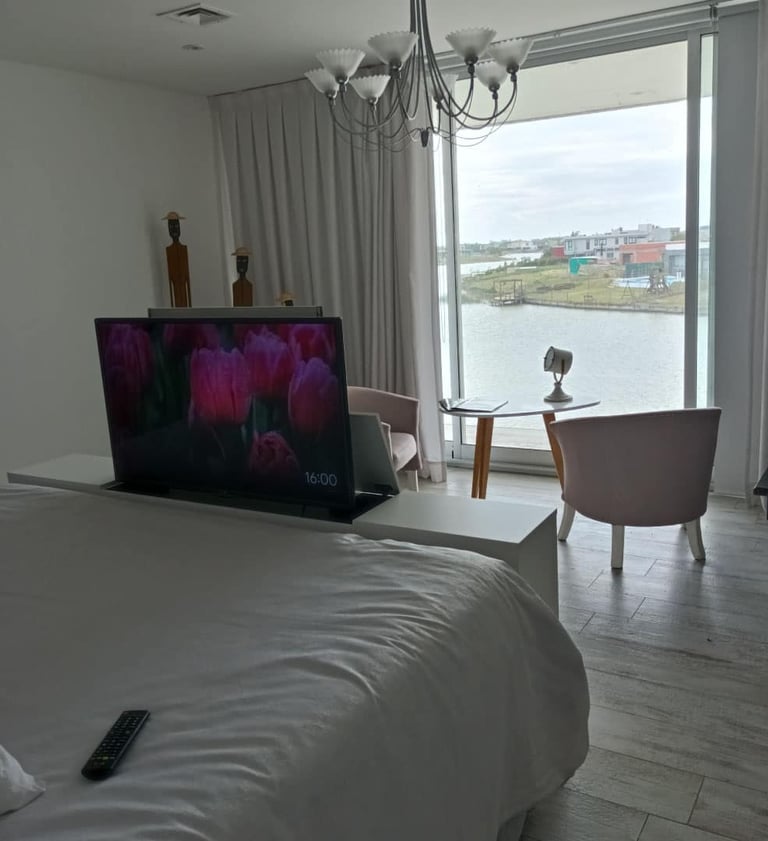 Mueble pie de cama con elevador de TV motorizado frente a ventanal en dormitorio moderno