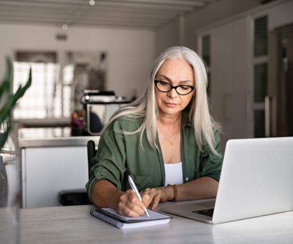a woman in glasses and a green shirt is sitting at a desk with a notebook