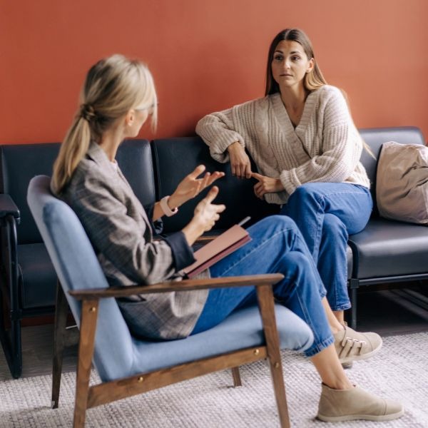 a woman sitting on a couch talking to another woman 